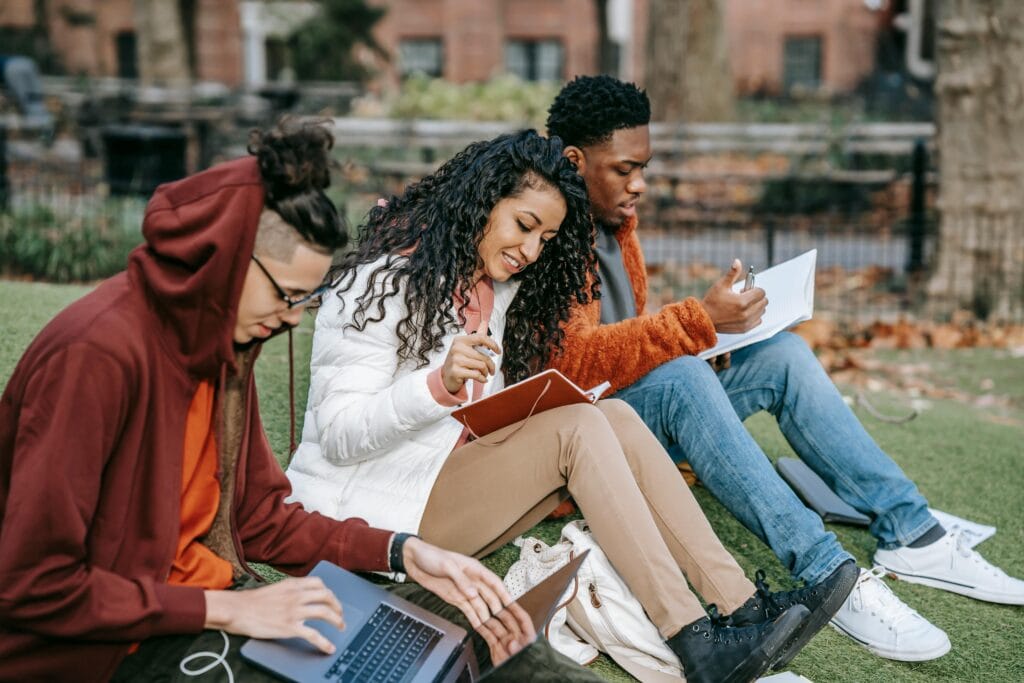 3 students studying outside computer books